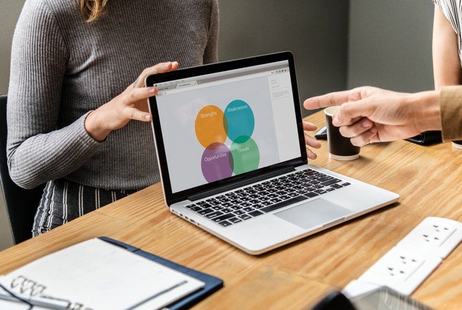 Businesswoman holds a laptop with a presentation while someone offscreen points to it.