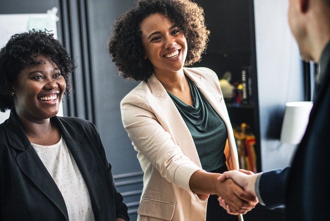 Image of two business women standing and shaking hands with male colleague