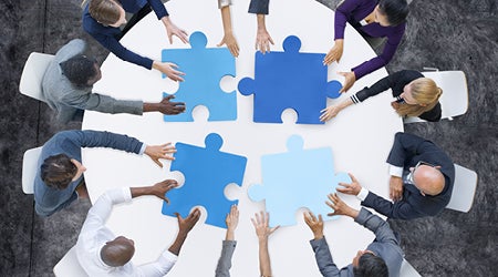 people around a table putting together four puzzle pieces