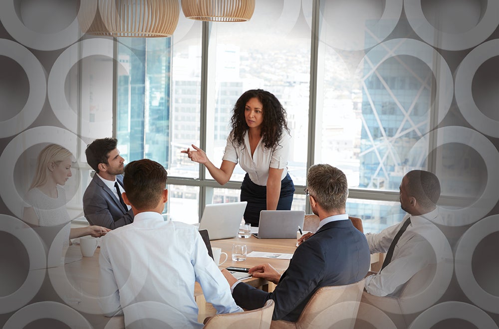 Diverse female professional speaking to a group of business colleagues sitting around a table in a conference room