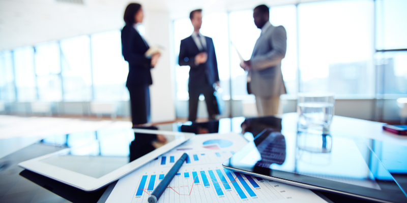 financial statements on a table with three business people in the background