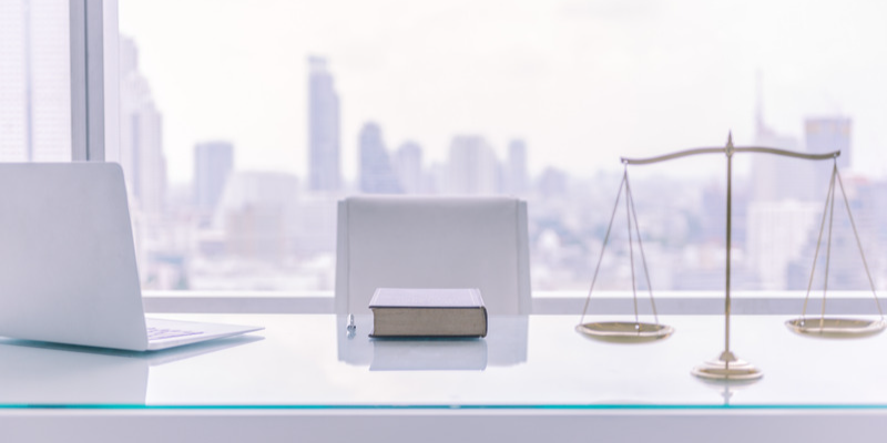 a laptop, book, and scales of justice on a desk in a corporate office