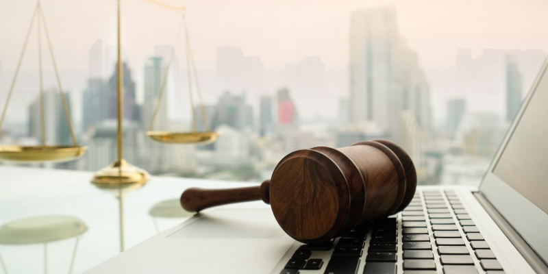 a gavel laying on a computer keyboard with the scales of justice in the background