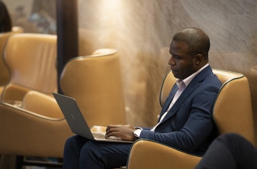 Professional dressed in suit and sitting in a yellow armchair and reading on a laptop in a convention center space
